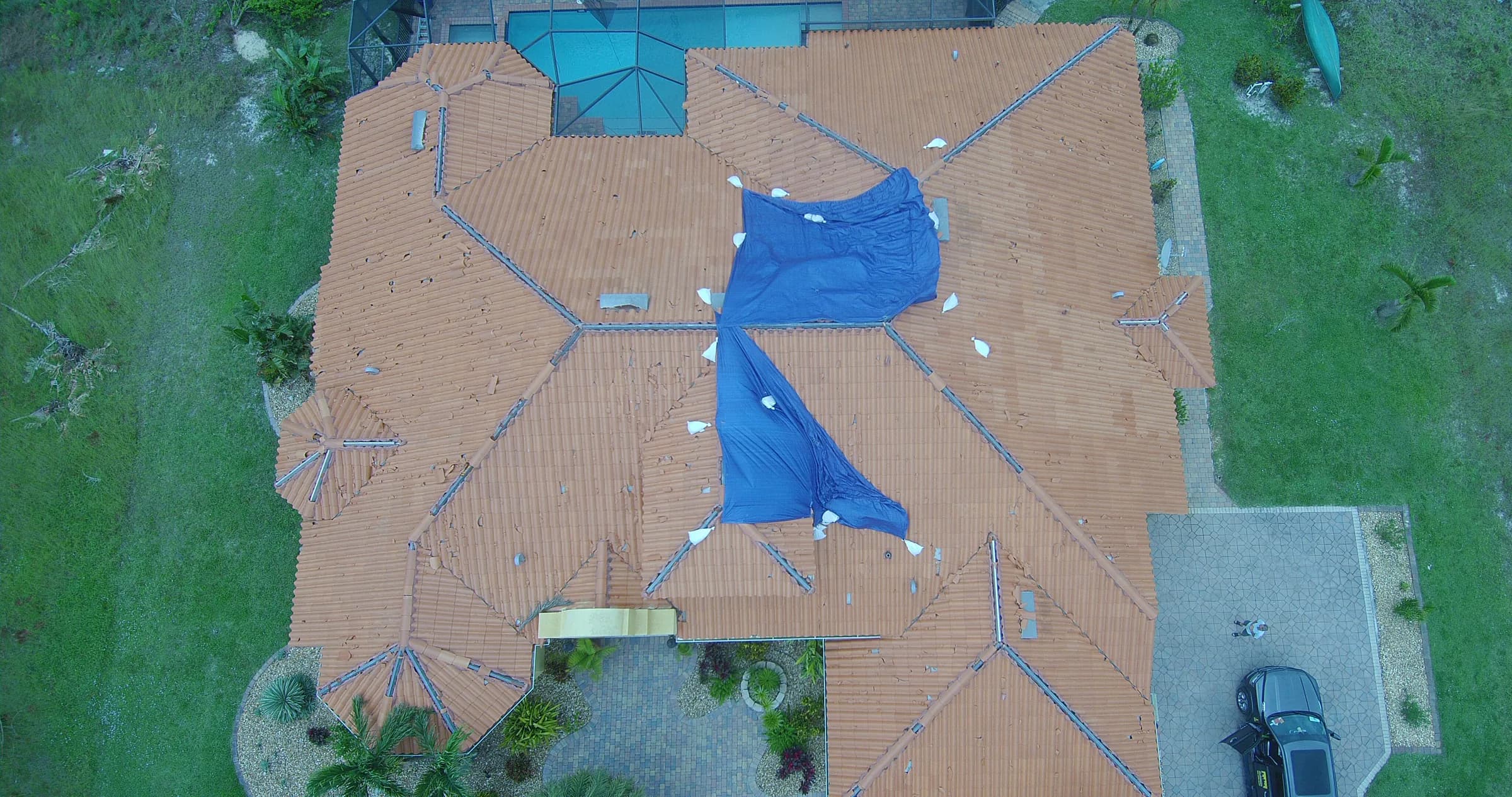 Overhead view of a storm-damaged clay tile roof with broken tiles and temporary tarps
