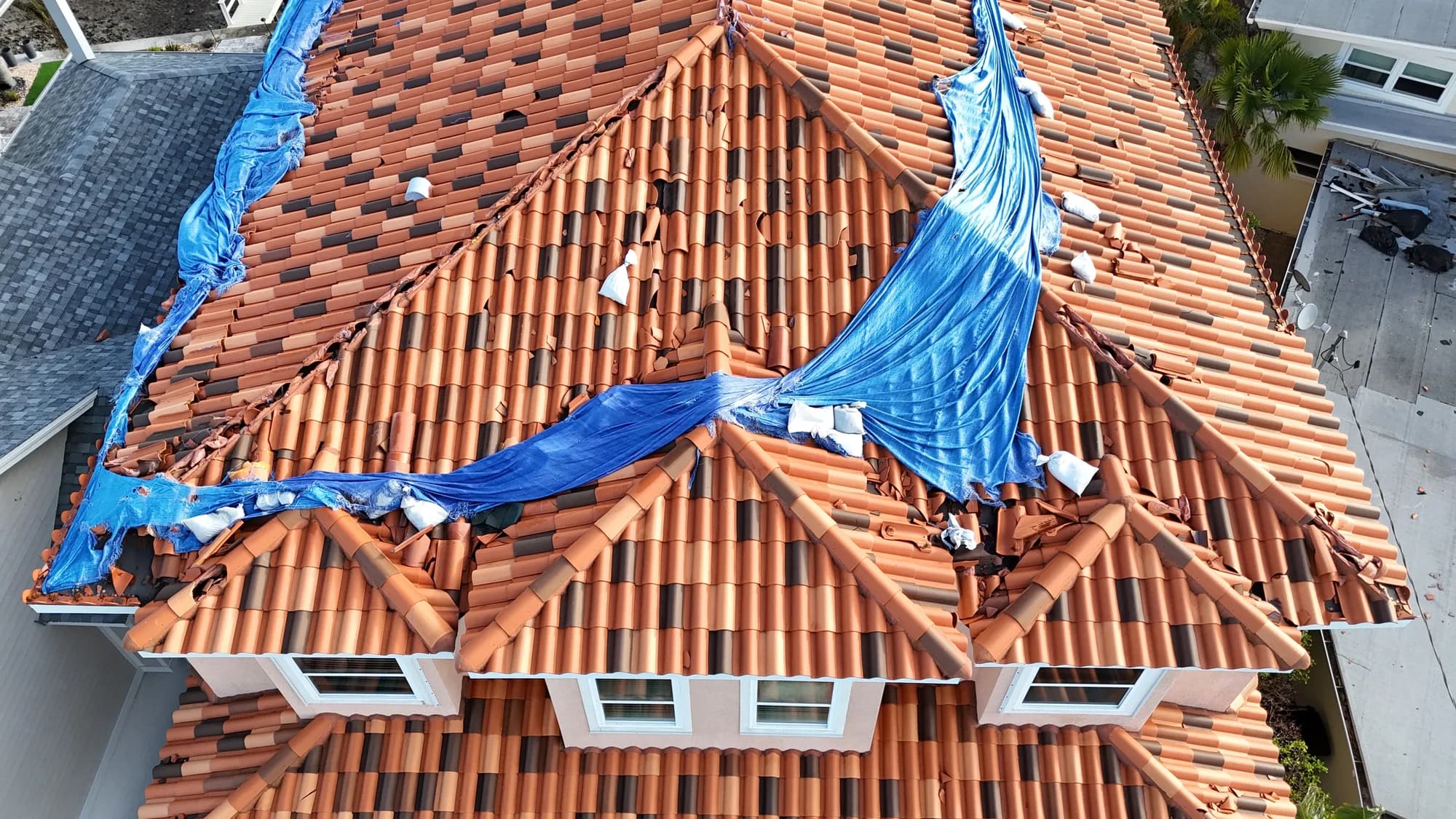 Drone view of a clay tile roof after a hurricane, with a shredded emergency tarp draped across the ridge