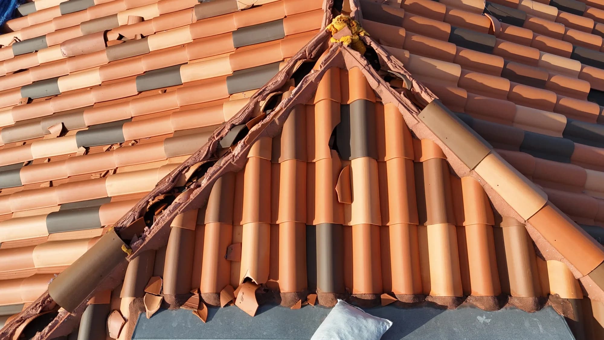 Close drone view documenting broken and displaced clay ridge tiles without anyone walking the roof