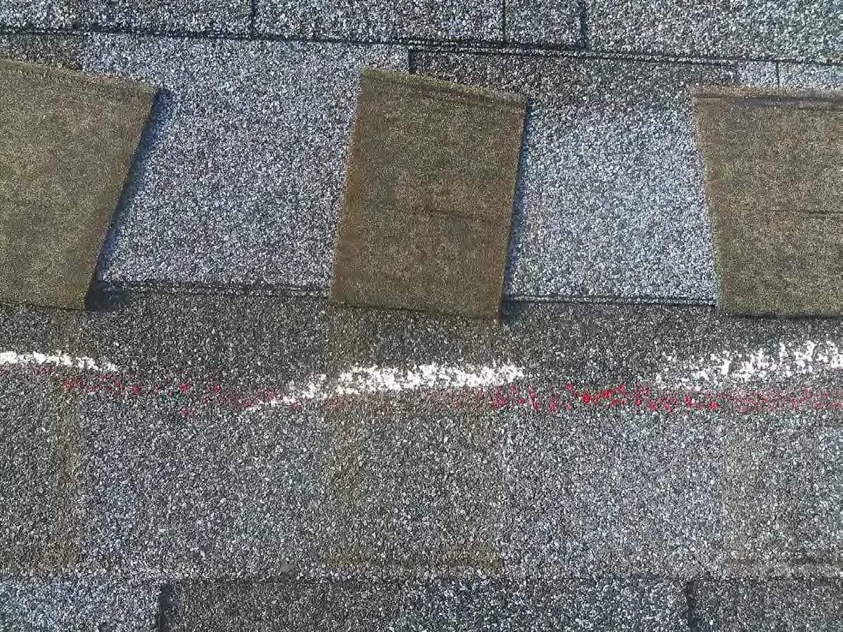Close-up of lifted, creased shingle tabs above a line of white and red inspection chalk.