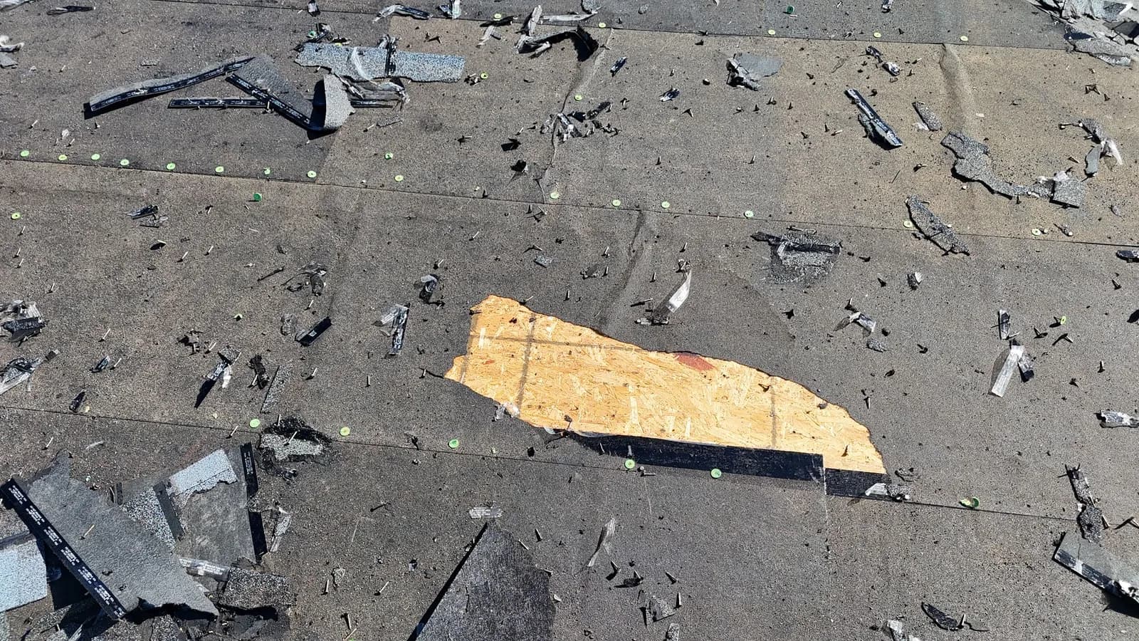 Roof deck at tear-off still covered by an older peel-and-stick membrane with cap nails, one patch of bare sheathing exposed, and shingle debris scattered across it.