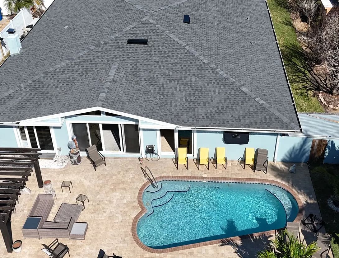 Aerial view from behind the house showing the finished charcoal shingle roof over the rear patio and pool.
