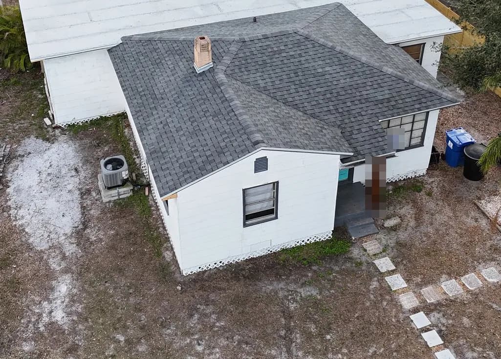 Aerial view of a one-story house with a new gray shingle hip roof and a bright white flat roof section behind it