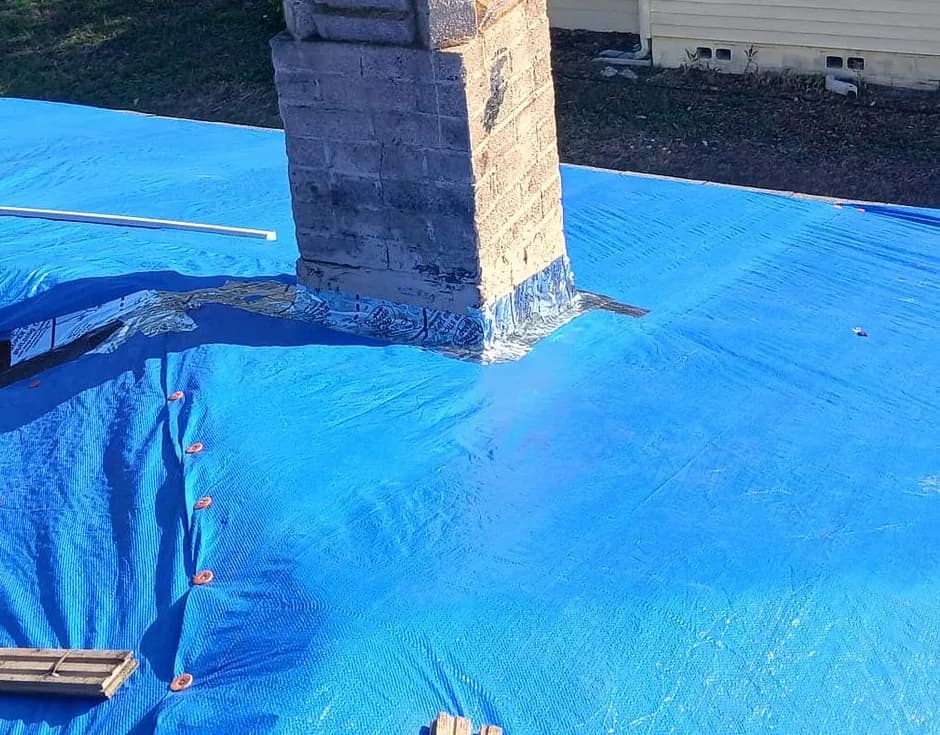 Blue tarp over a roof slope with a concrete block chimney wrapped in membrane at its base