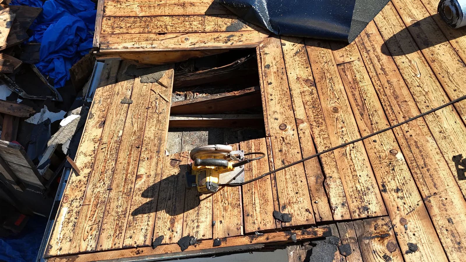 Cut-open section of rotted plank roof decking with a circular saw resting beside the opening