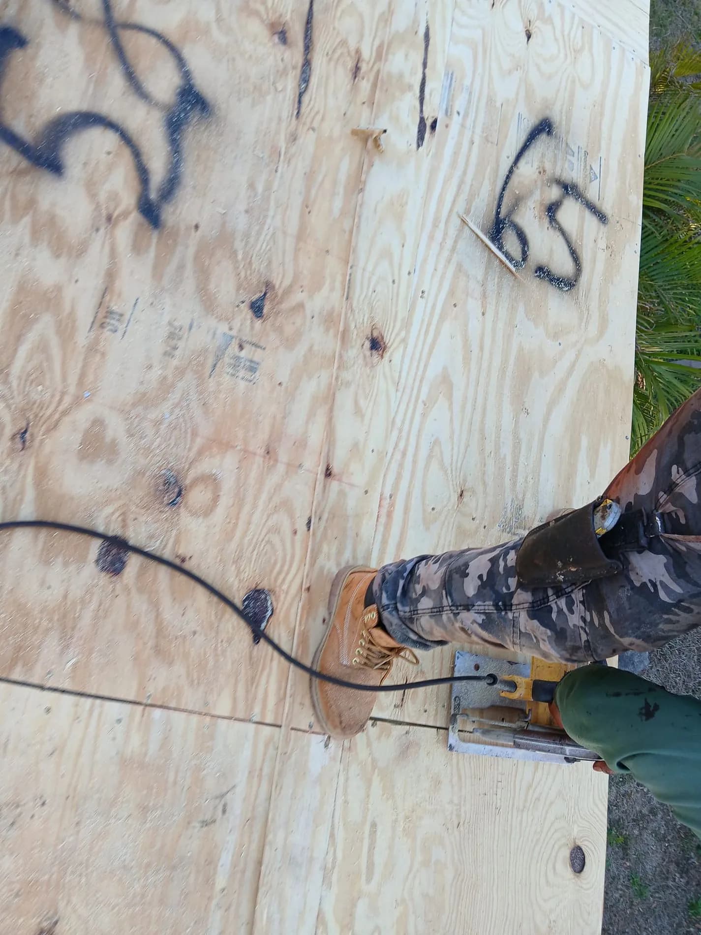 Worker cutting a sheet of new plywood roof decking marked with spray-painted numbers