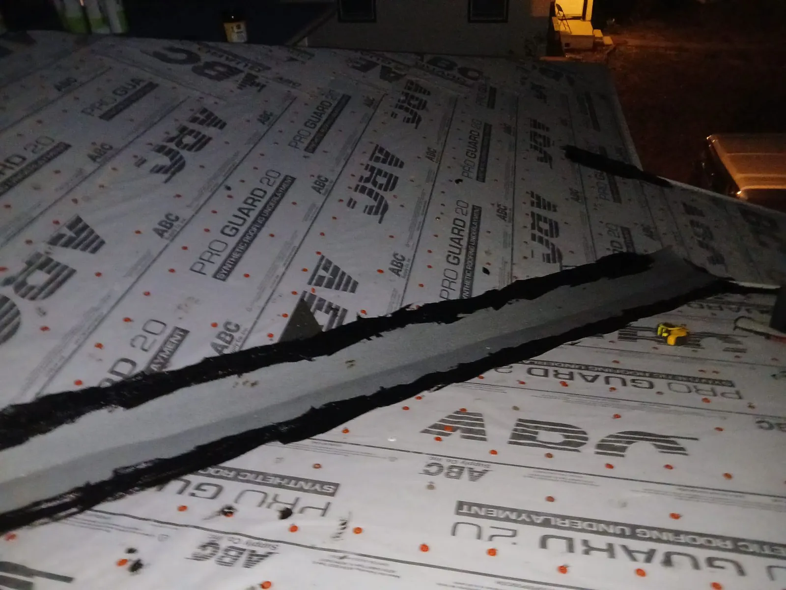 Gray synthetic roofing underlayment fastened with cap nails across a roof at dusk