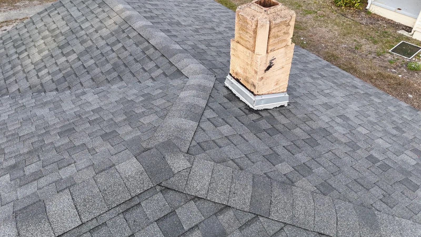 Finished gray shingle roof with woven hips and a sand-colored block chimney with new metal counterflashing
