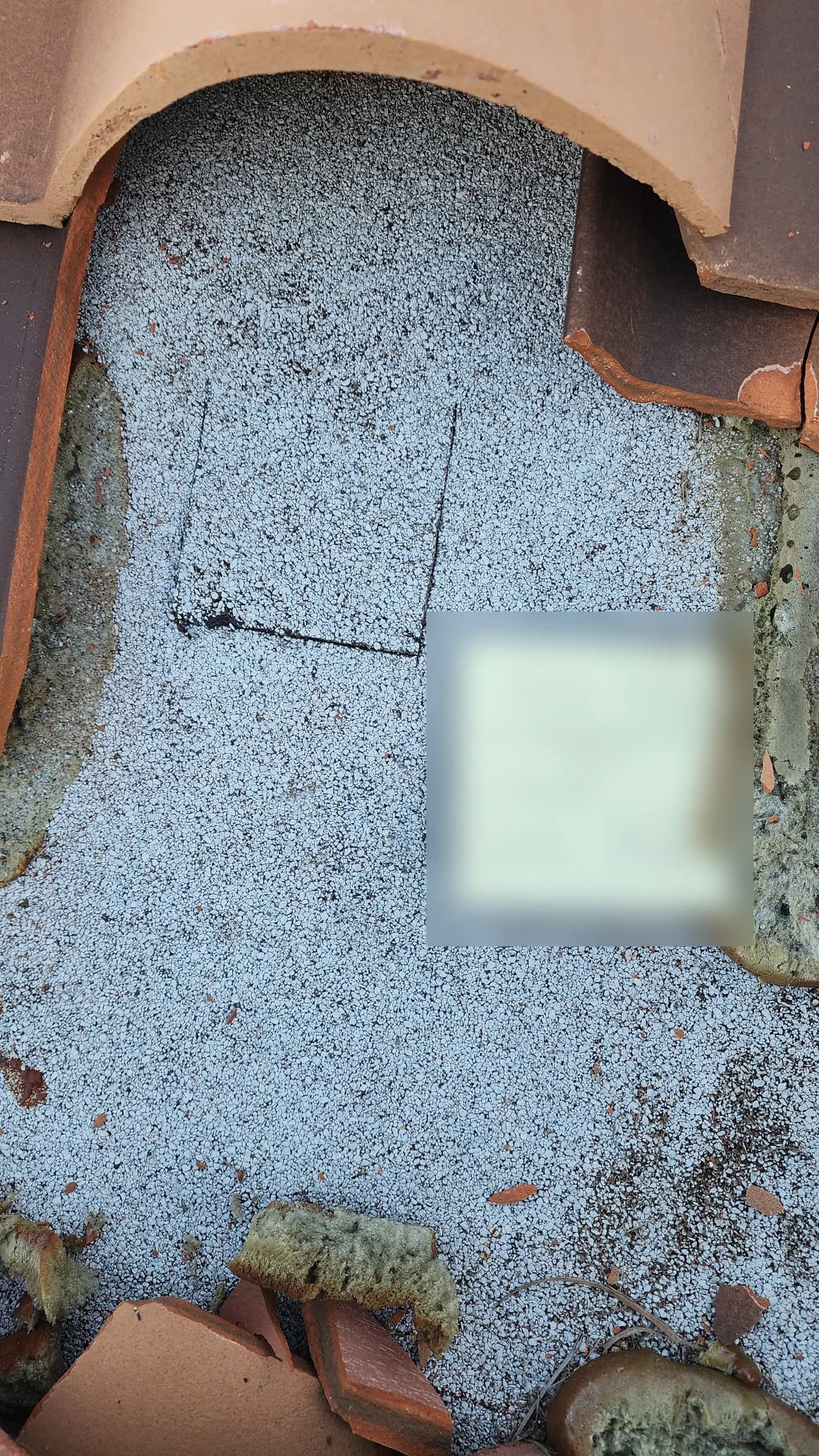 Close-up of a square core-test cut in gray granulated underlayment surrounded by removed clay tile pieces