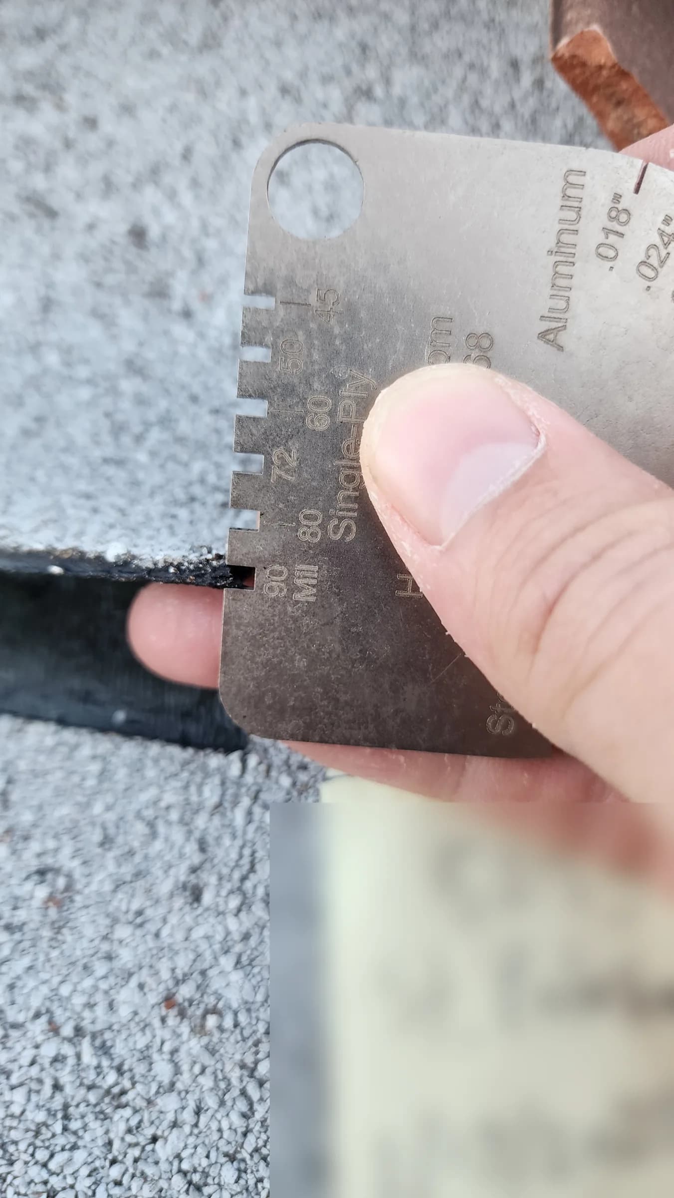 Thickness gauge held against the cut edge of gray granulated roof underlayment