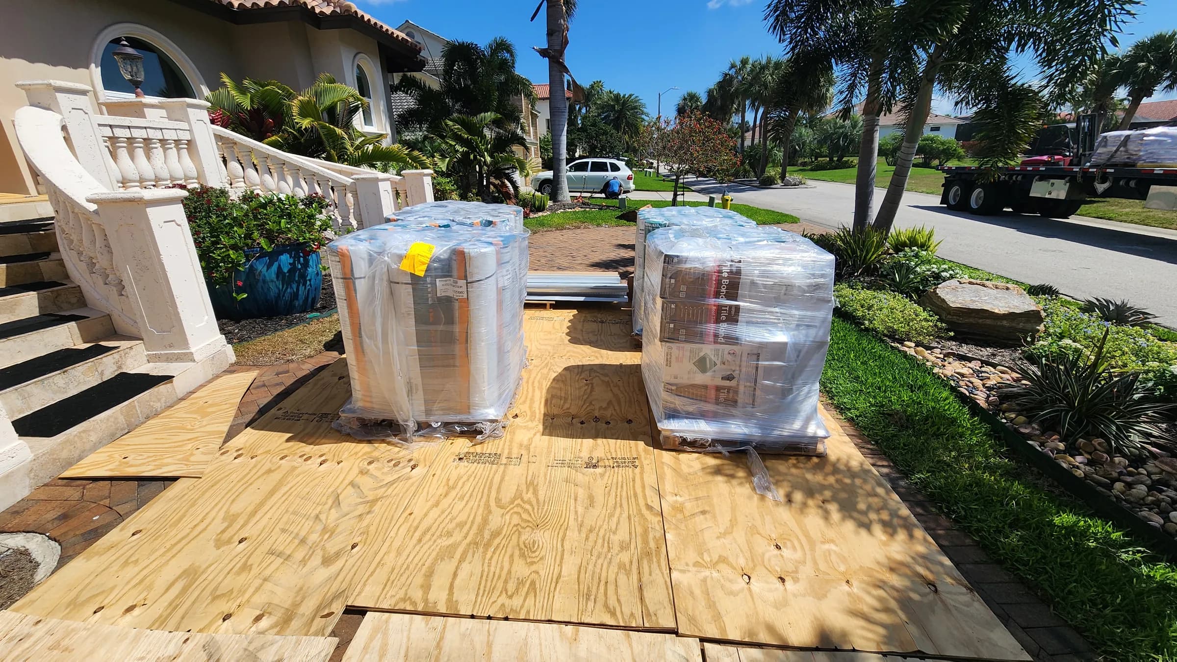 Wrapped pallets of underlayment staged on plywood covering the clay brick driveway