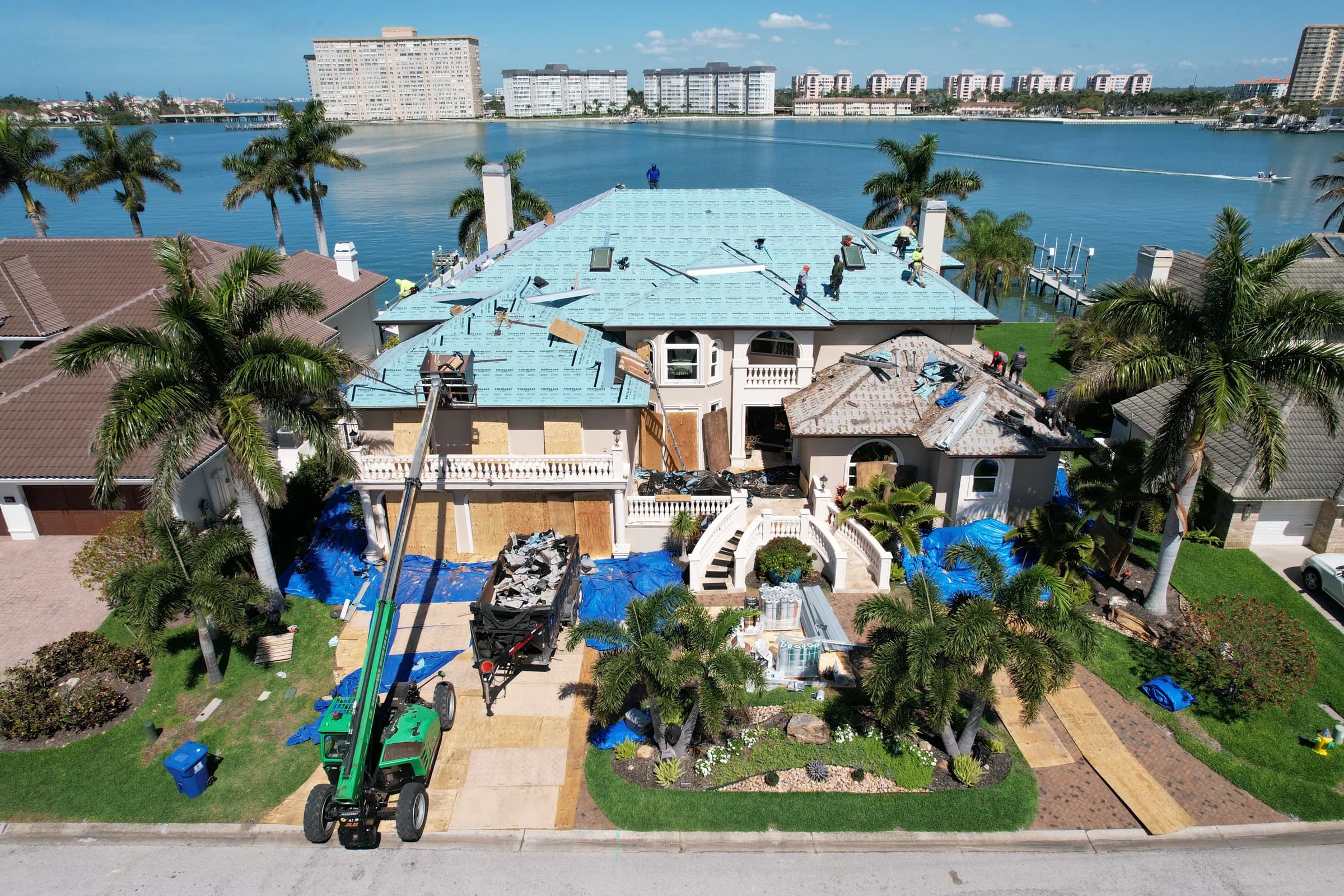 Front aerial view of crews installing teal underlayment across the main roof while tear-off continues on a lower section