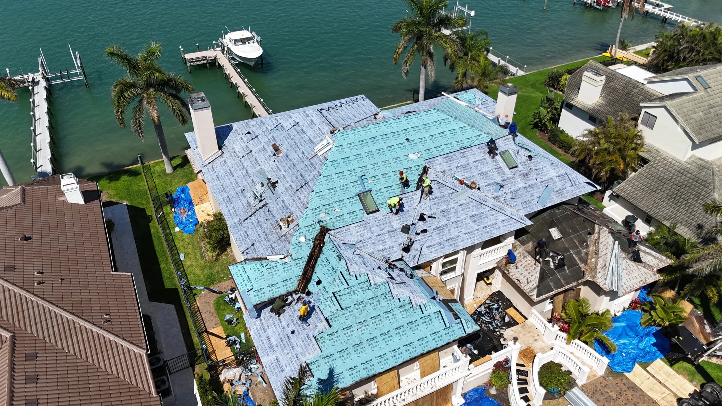 High aerial view of teal base sheet and gray cap sheet advancing across multiple roof slopes