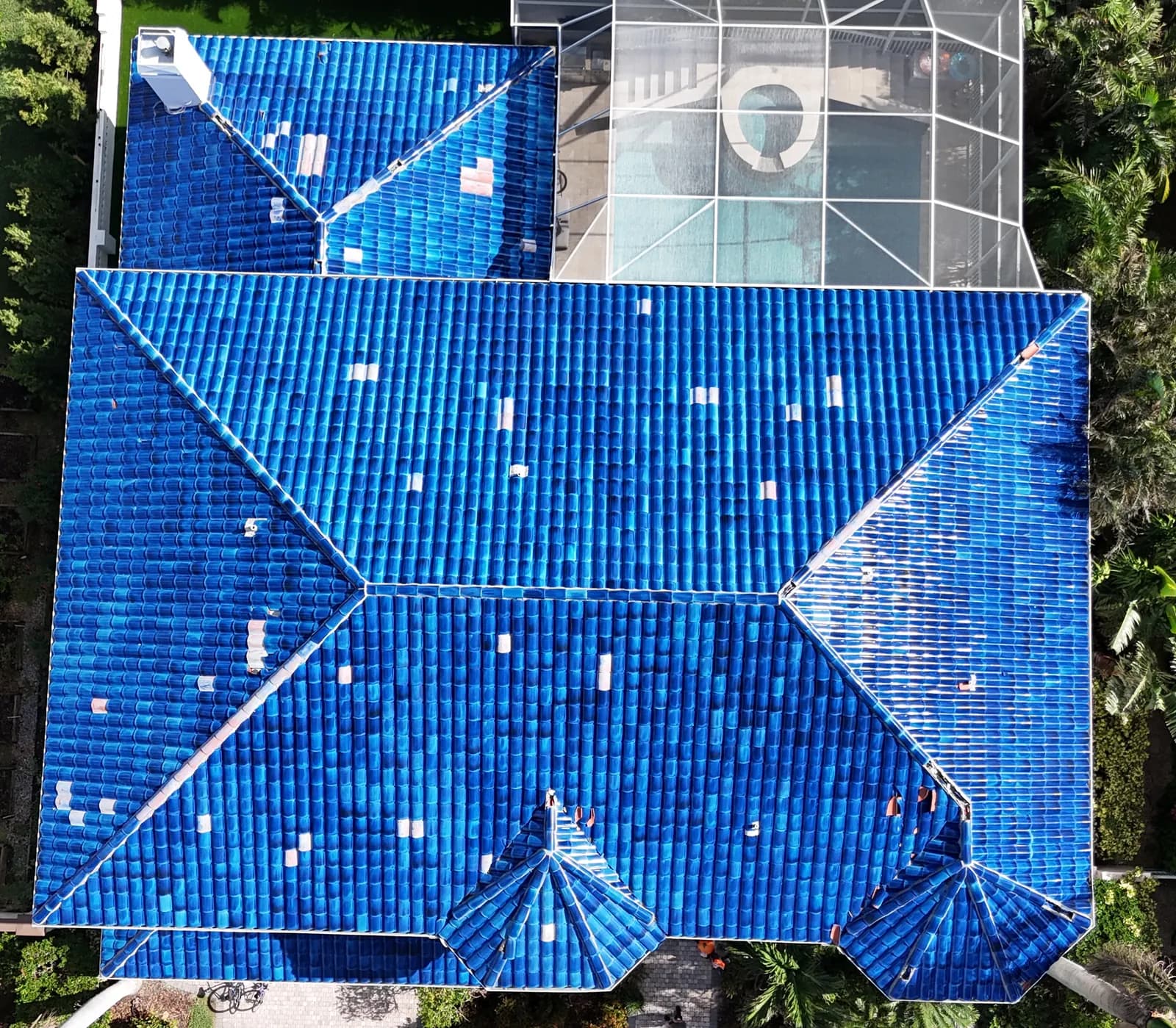Straight-down aerial of the glazed cobalt blue clay tile roof before the conversion, with lighter mismatched repair tiles scattered across the slopes.