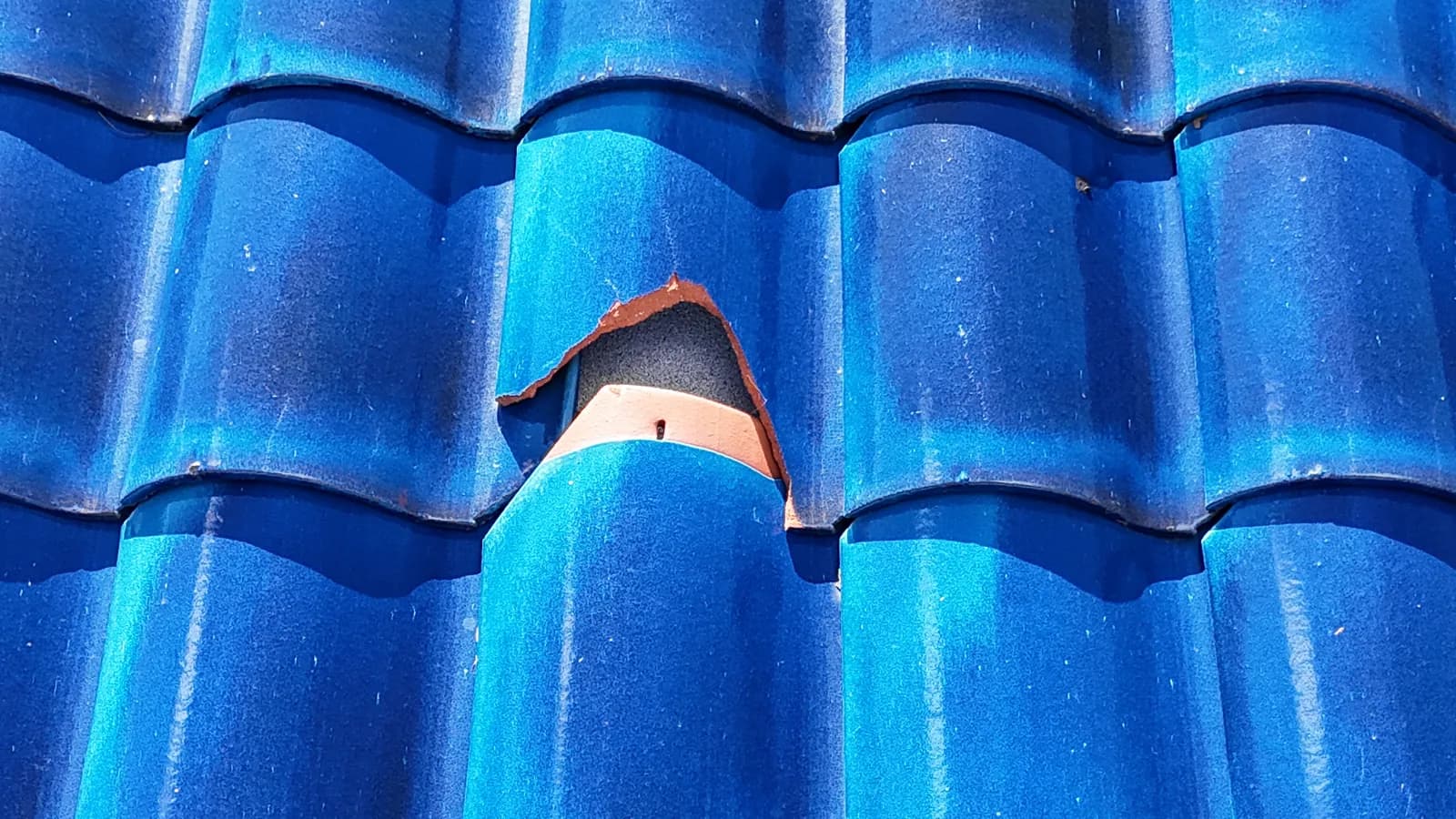 Close-up of a punctured blue clay tile with a hole broken through to the layers beneath.