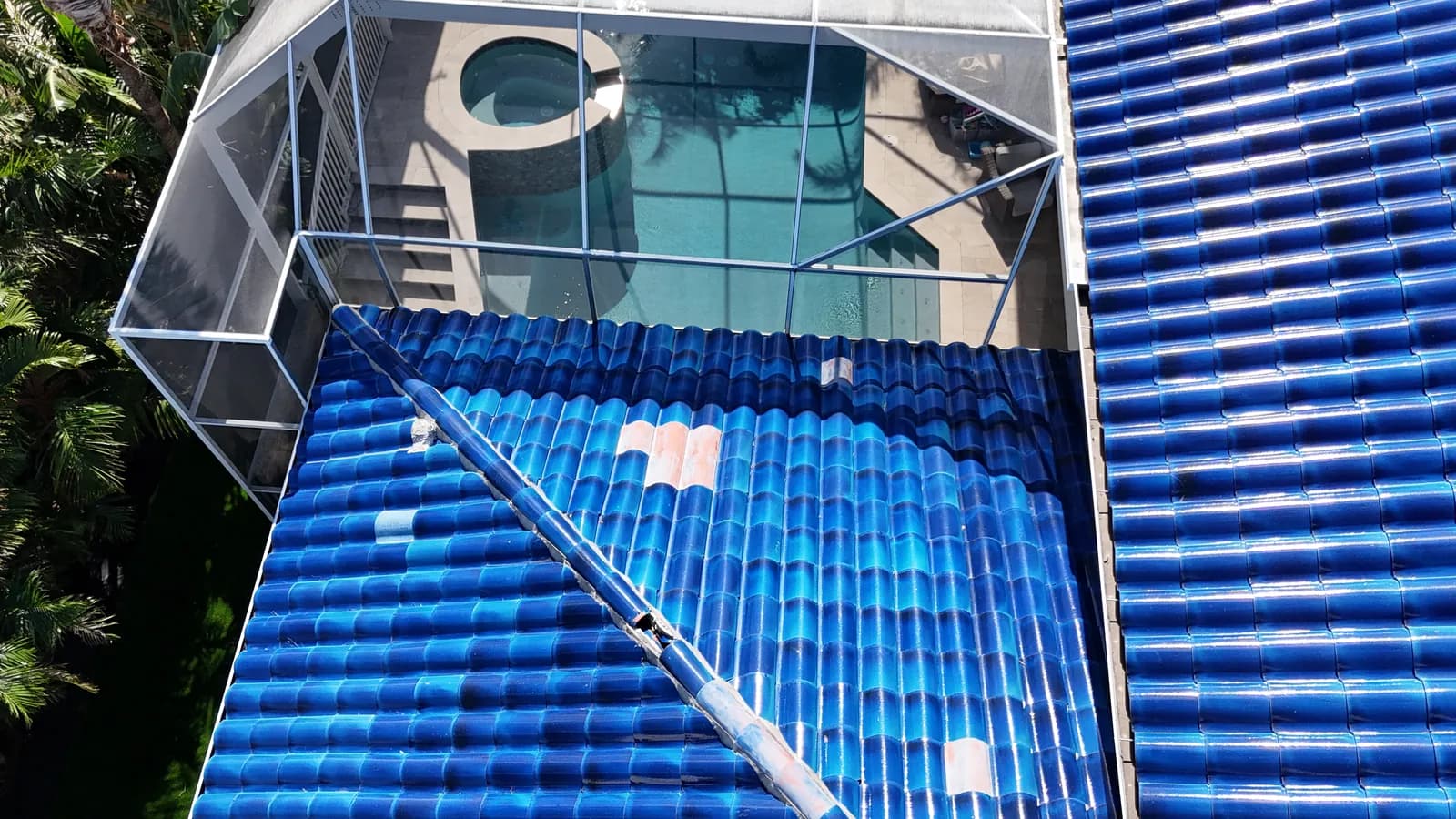 Displaced hip cap tiles and broken mortar on a ridge line above the screened pool enclosure.