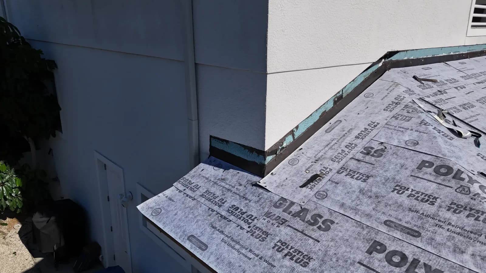 Stucco cut back at a second-story wall corner, with new dark metal flashing set over the underlayment to counterflash behind the stucco.