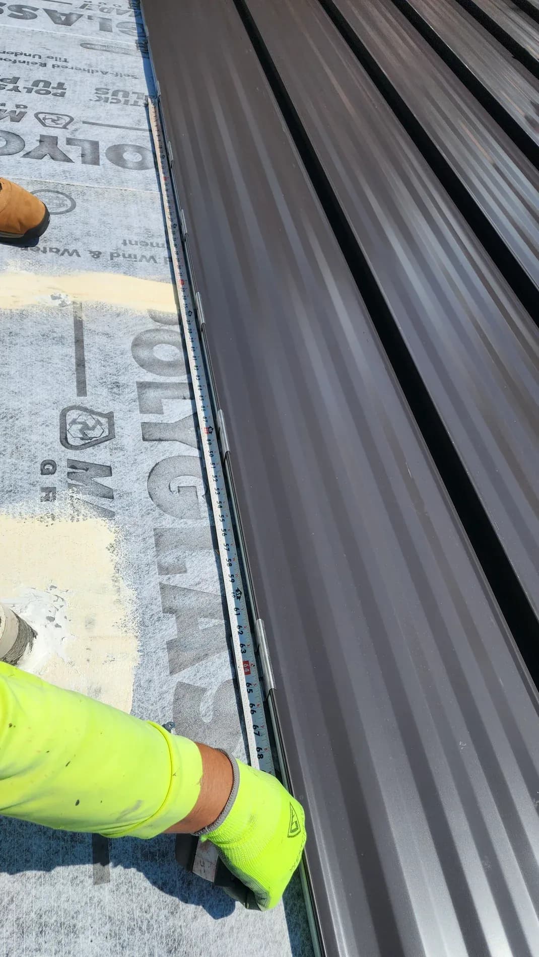 A gloved hand setting a snaplock standing seam panel over branded underlayment, with the line of metal clips along the seam.