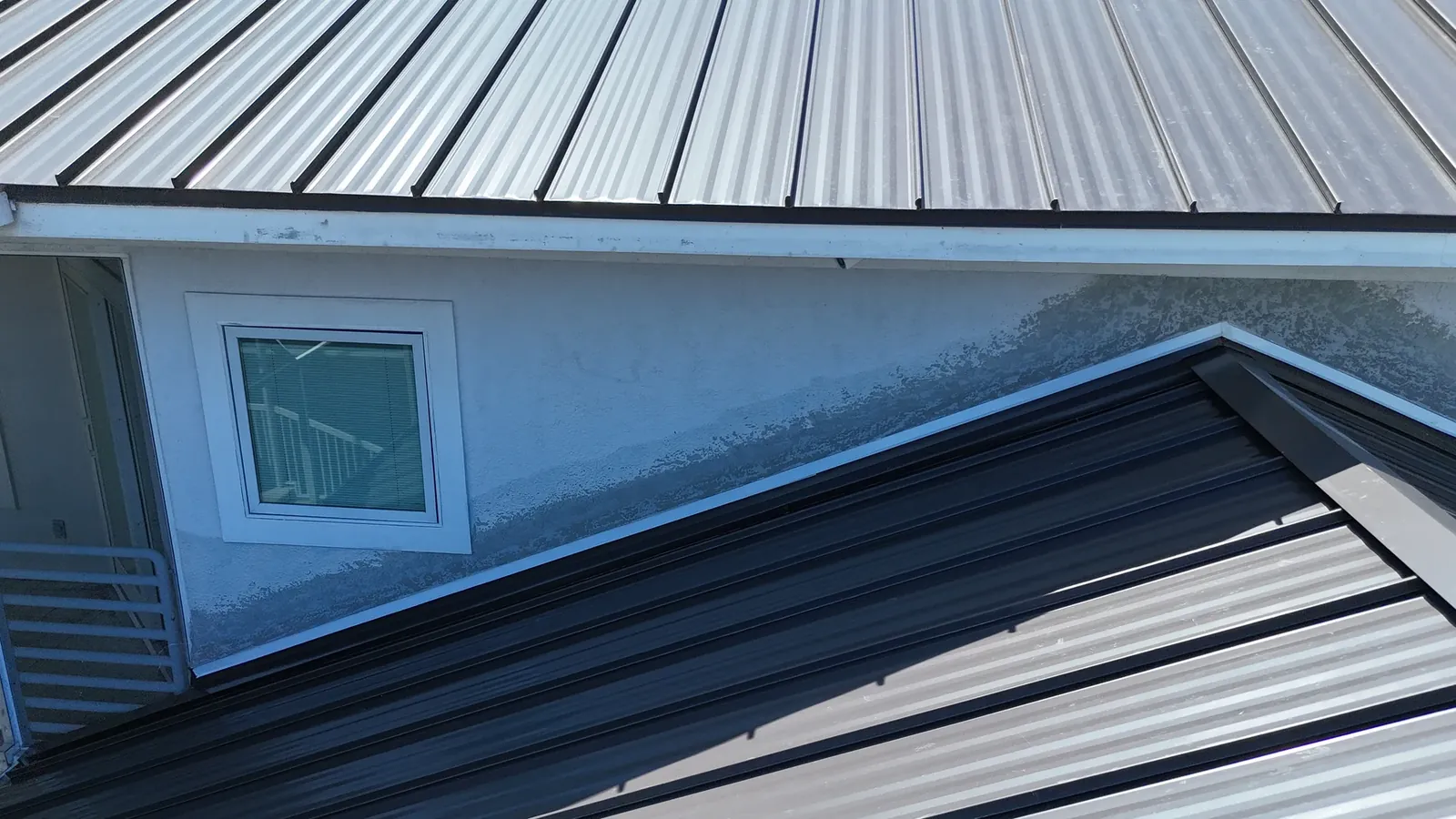 Finished standing seam panels meeting a second-story wall, with straight seam lines and new flashing at the transition.