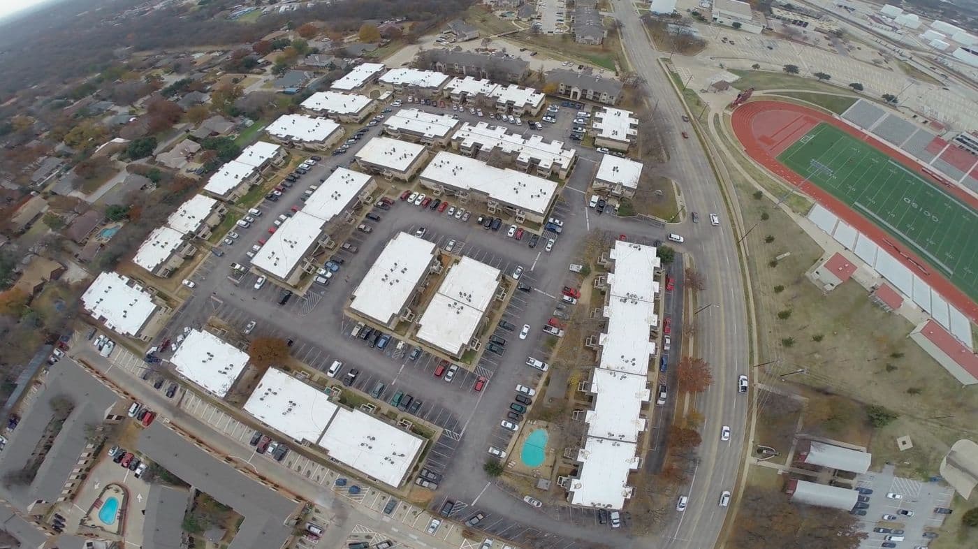 Aerial view of a multi-building apartment complex with new white low-slope roofs, parking lots, and a pool.