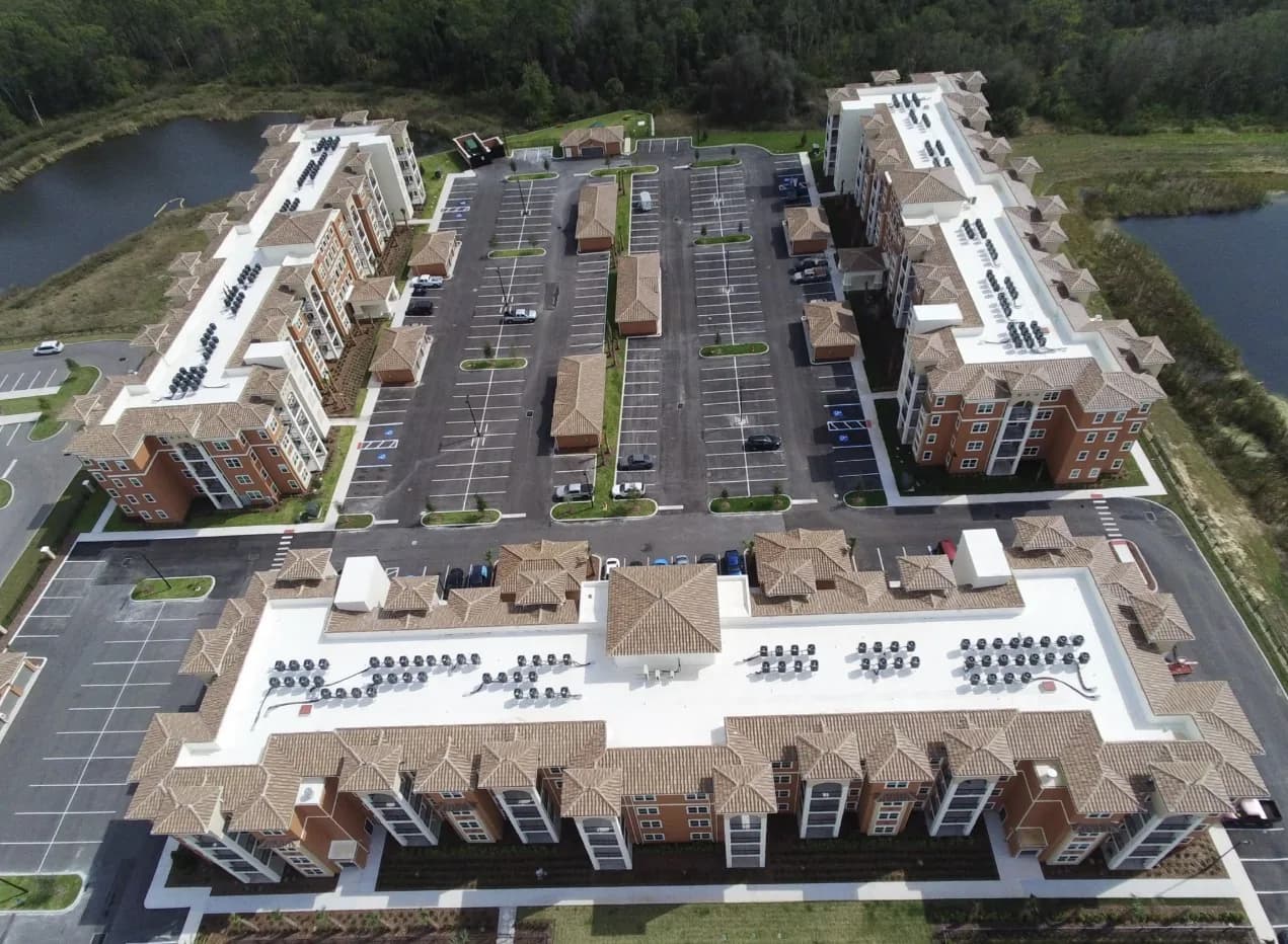 Aerial view of a large commercial complex with white TPO roof fields and tan tile roof sections