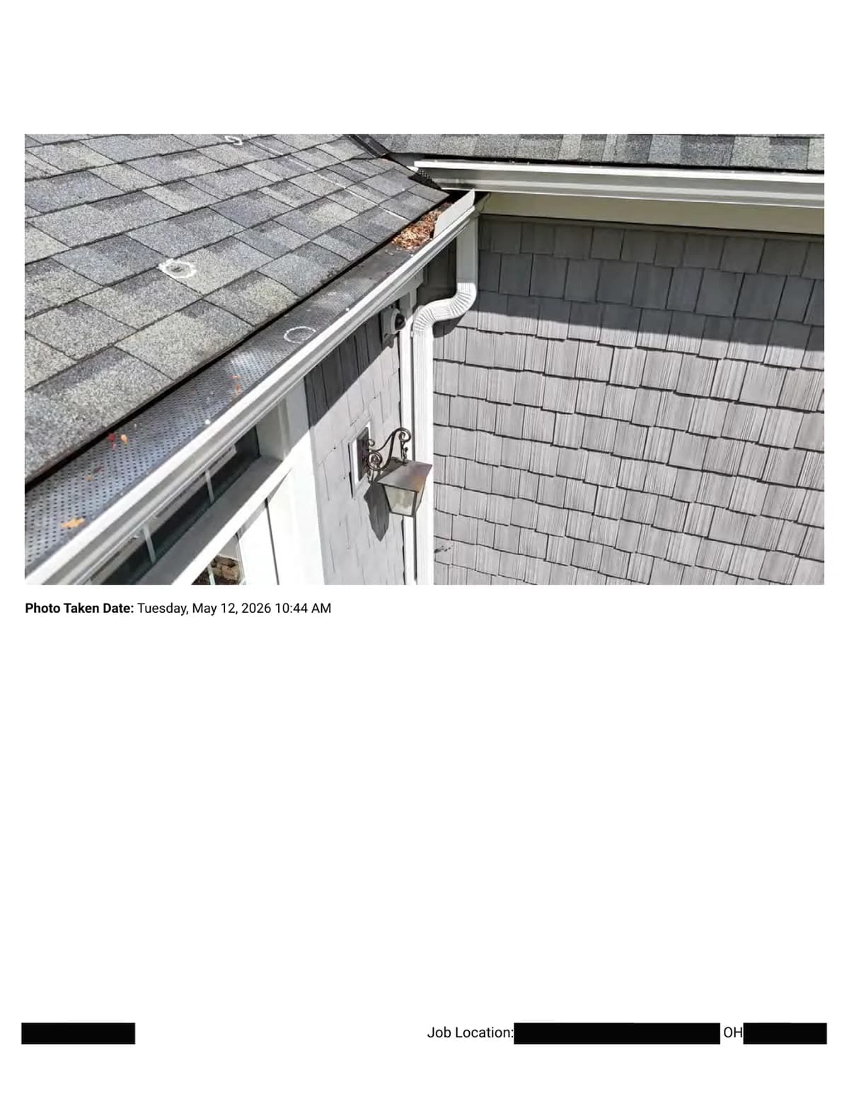 An eave corner: gutter with perforated guard, downspout, and wall shingles, with a chalk circle marking an impact on the roof slope above.