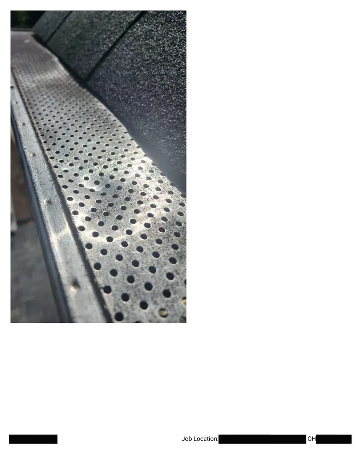 Close-up of a dent in the perforated metal gutter guard, evidence of hail impact on metal.