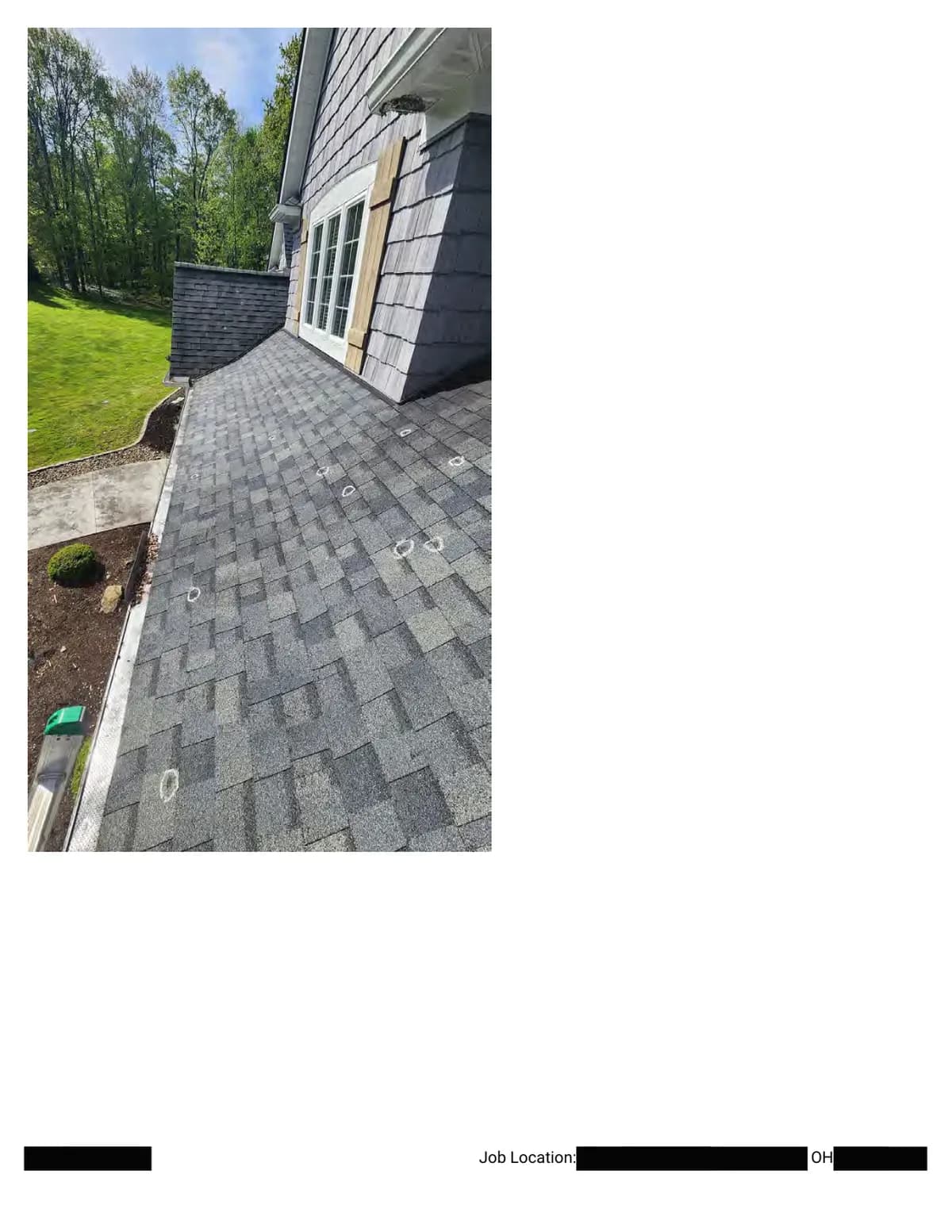 Looking down a lower slope with several hail impacts circled in chalk; the yard and landscaping are visible past the eave.