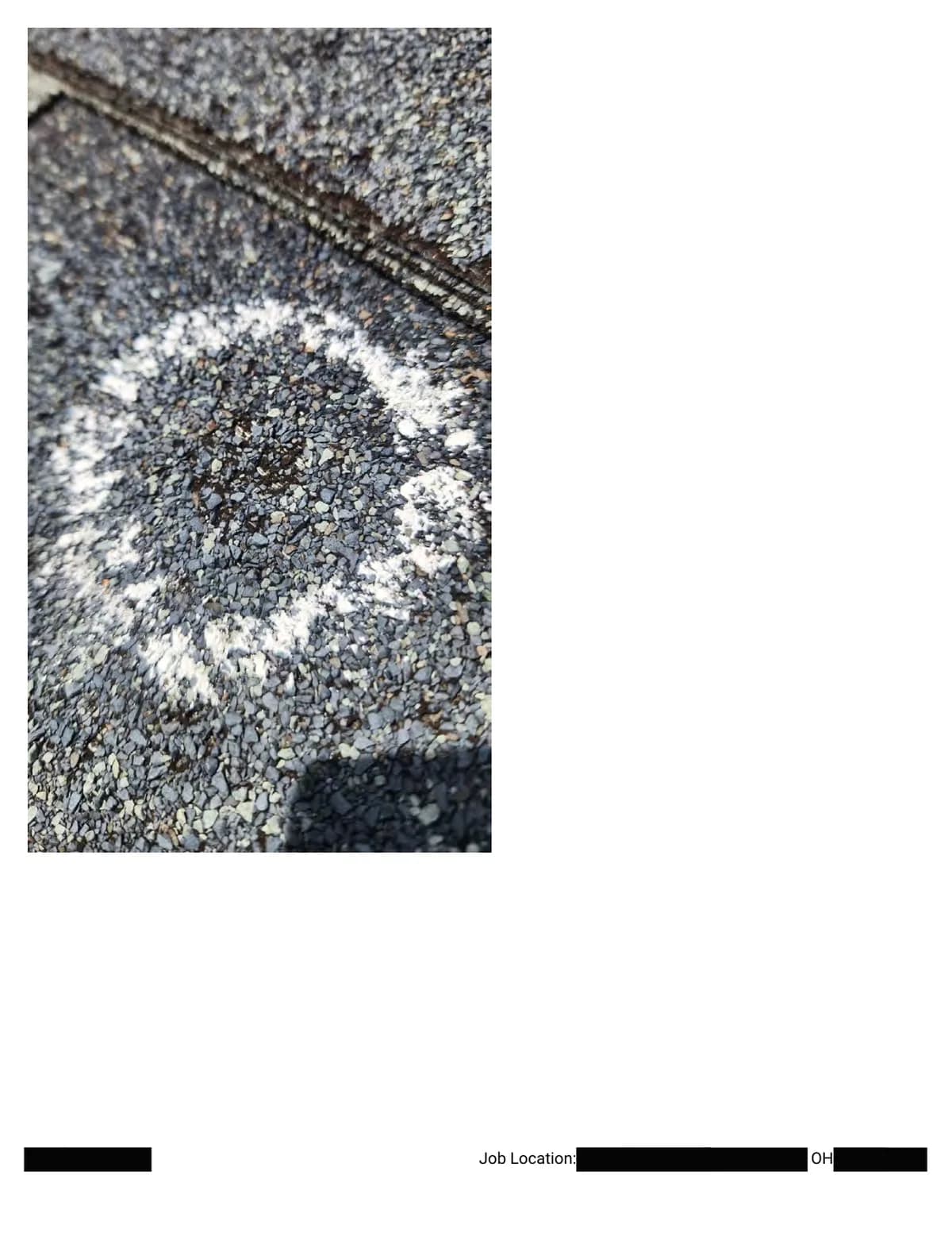 Extreme close-up of a chalk ring around a hail impact, granules crushed to the dark asphalt at the center.