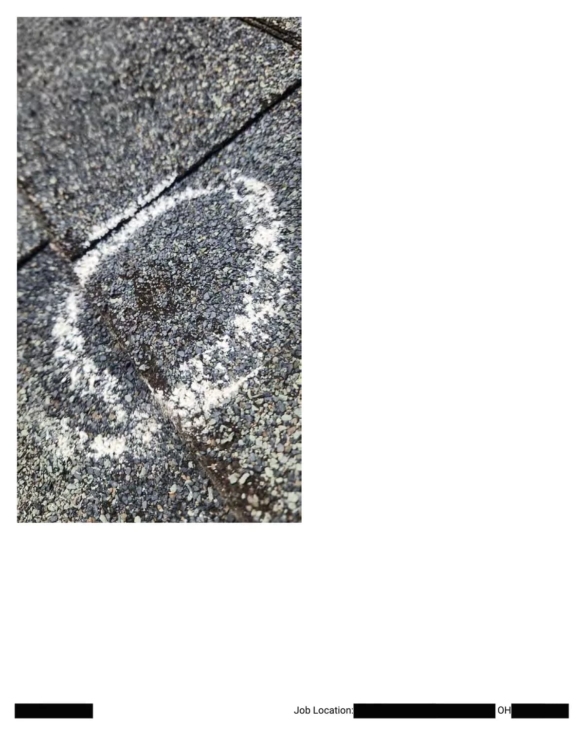 Extreme close-up of a chalk circle around a broad hail bruise crossing a shingle edge.