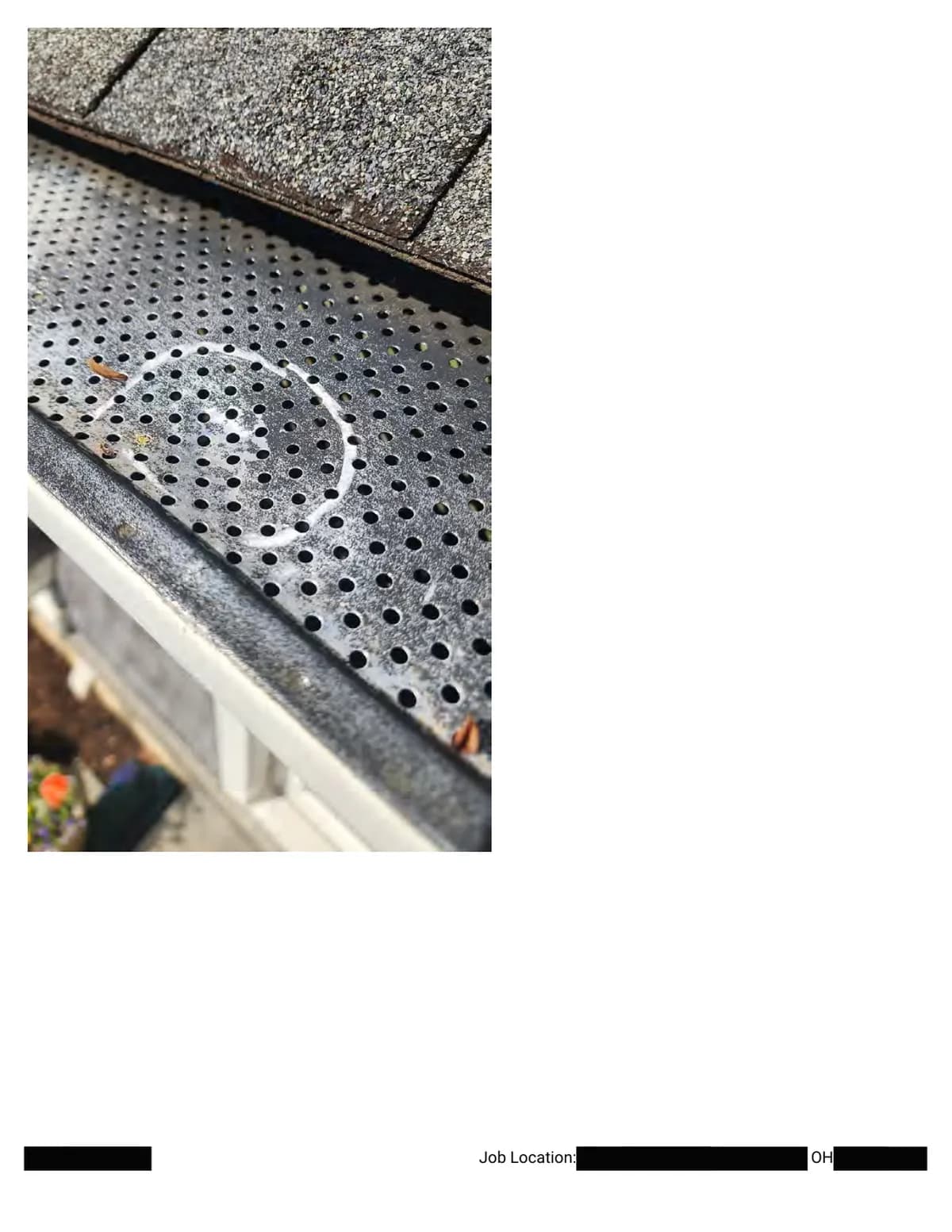 Close-up of a chalk circle drawn around a dent in the perforated metal gutter guard.