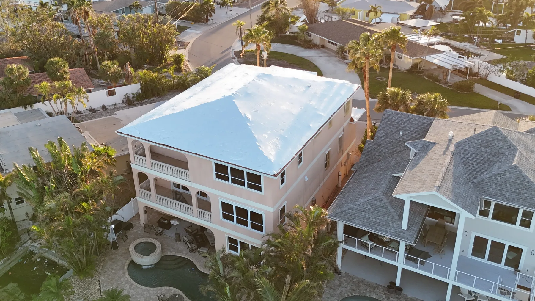 Aerial view of the same coastal home with its roof fully sealed in white shrink wrap