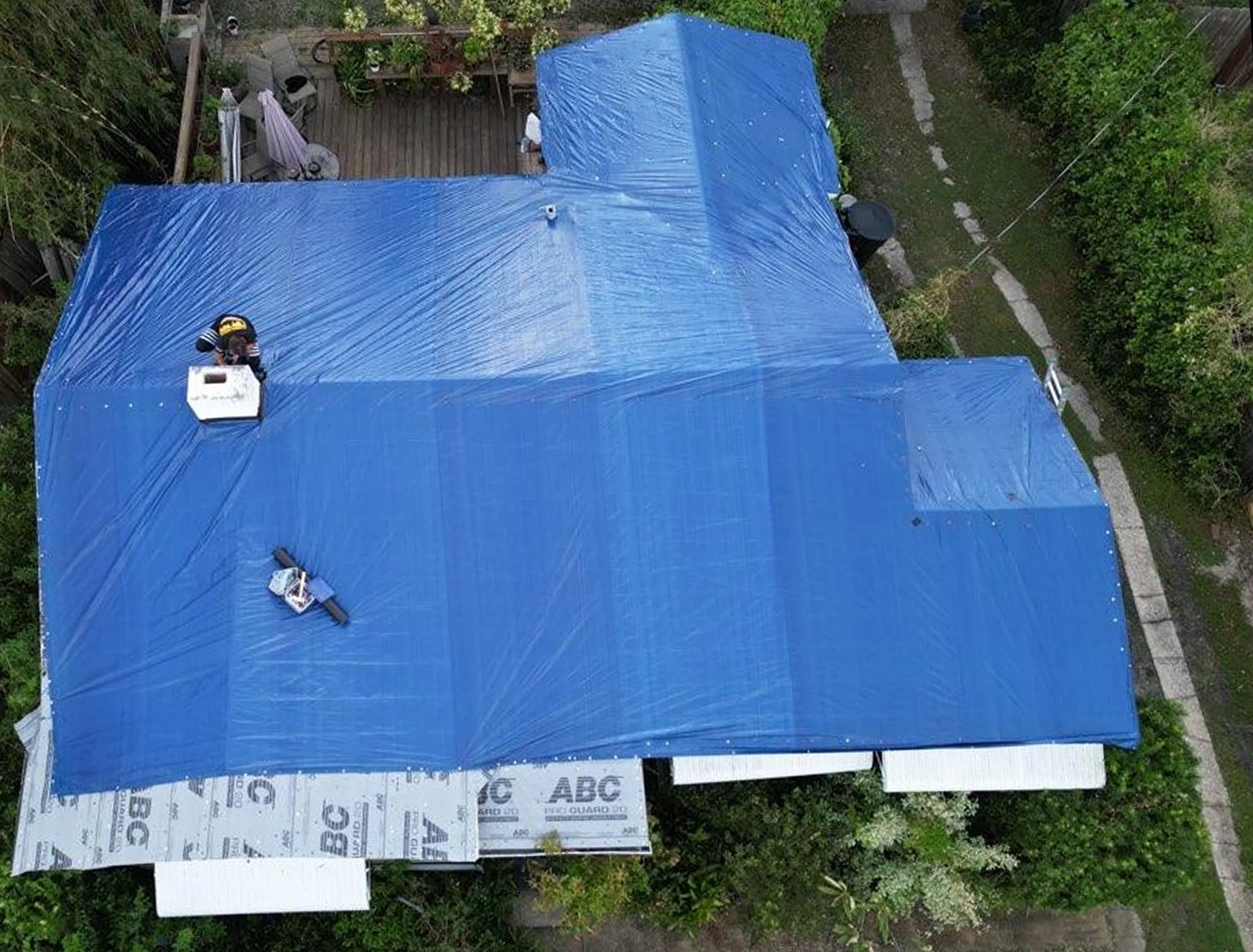 Overhead view of a blue storm tarp covering most of a residential roof
