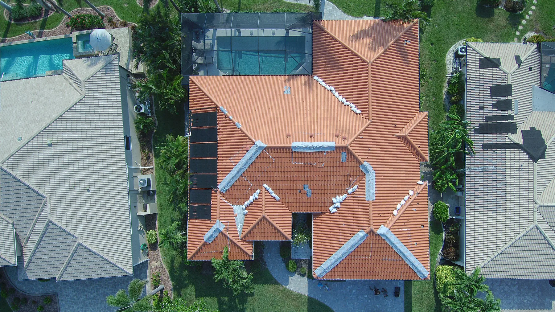 Overhead drone view of a Cape Coral clay tile roof with storm-damaged ridge and hip lines under temporary weatherproofing