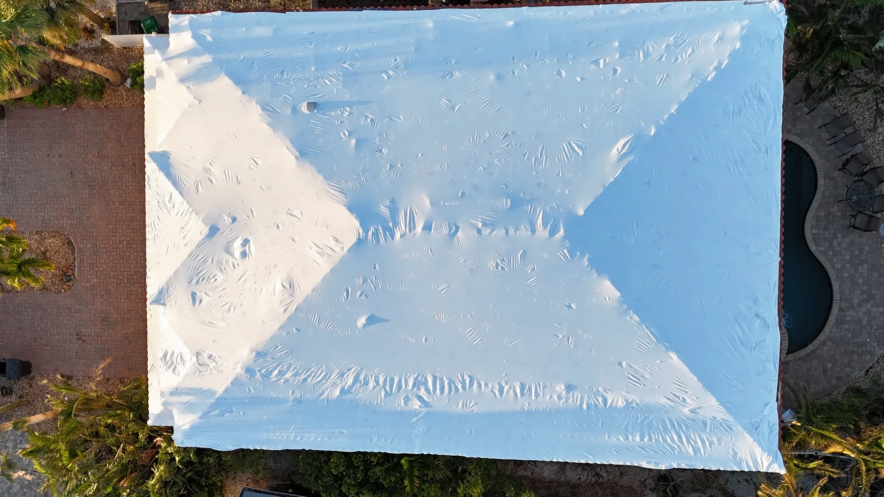Overhead drone view of the same tile roof fully protected by a white shrink wrap system