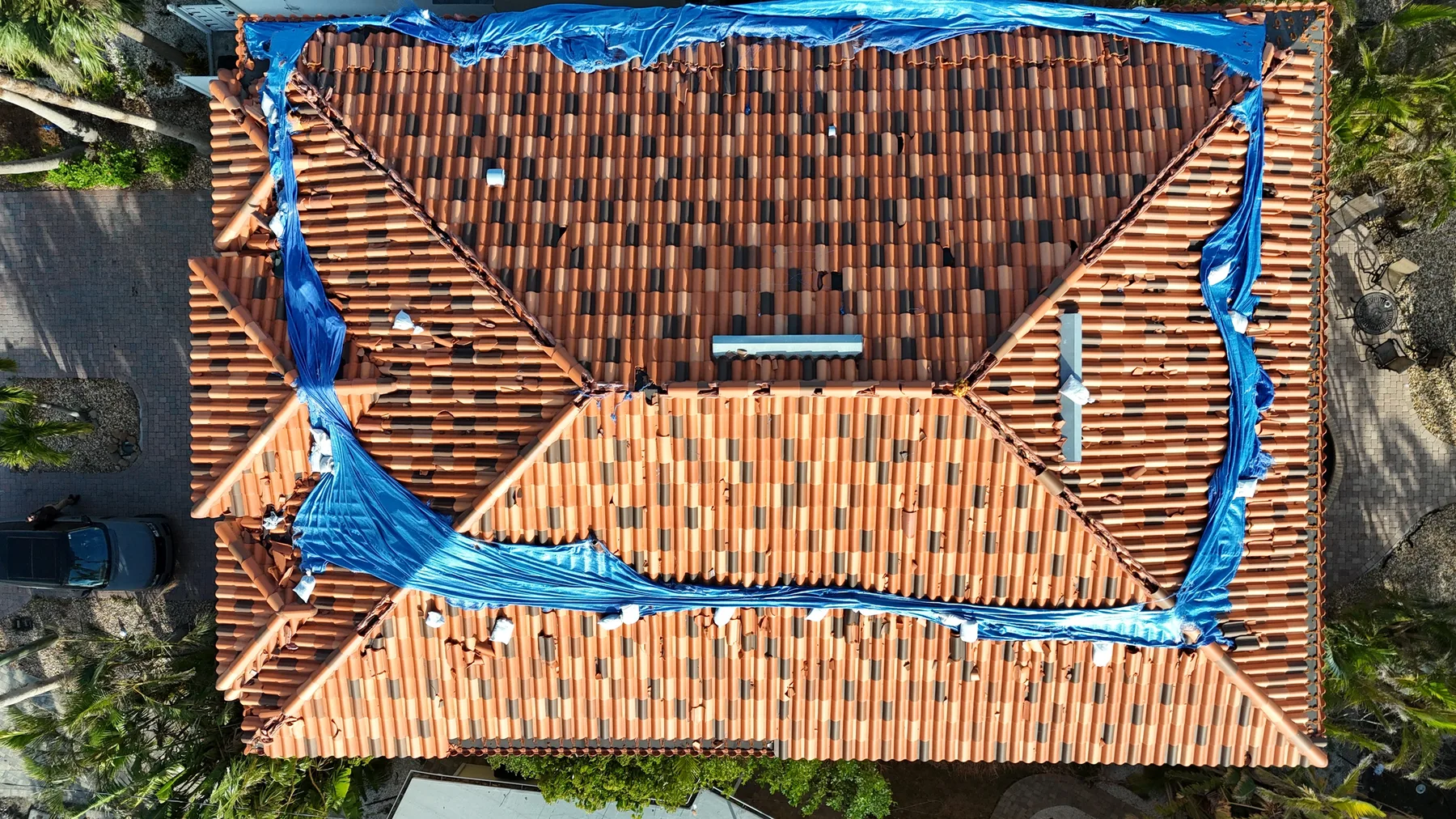 Overhead drone view of a storm-damaged clay tile roof with a shredded emergency tarp